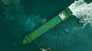 tugboat-dragging-cargo-ship-leaving-shipyard-after-repairs-green-sea-aerial-top-view-from-drone